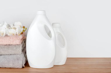 Deterjan şişeleri, yumuşatıcı, temiz havlular ve tahta masanın üzerinde orkide çiçekleri. Temizlik ürünleri konteynırları. Sıvı deterjan ve krem. Çamaşır günü, temizlik konsepti