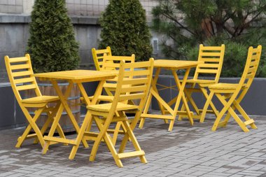Açık kafede ya da restoranda boş sandalyeler. Kaldırımdaki kafede sarı ahşap masalar ve sandalyeler