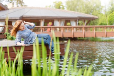 Genç bayan dinleniyor ve parkta eğleniyor. Gölün üzerindeki iskelede oturuyor.