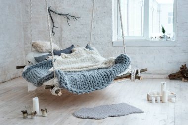 Beyaz çatı katı, klasik İskandinav tarzı. Tavandan sarkıtılmış yatak. Büyük, katlanmış gri ekose kumaş, dev örgü battaniye, süper tombul iplik, kol örgüsü. Moda oda tasarımı