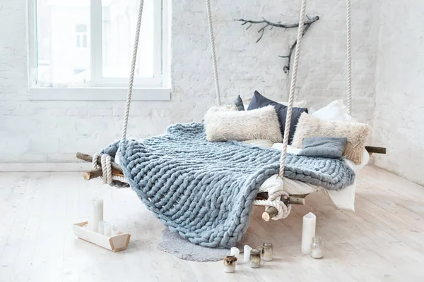 White loft interior in classic scandinavian style. Hanging bed suspended from the ceiling. Cozy large folded gray plaid, giant knit blanket, super chunky yarn, arm knitting. Trendy room design