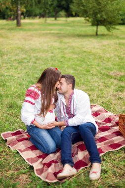 Ulusal Ukrayna tarzı giyinmiş genç ve güzel bir çift sonbahar parkında piknik yapıyor. Annelik ve aile mutluluğu kavramı