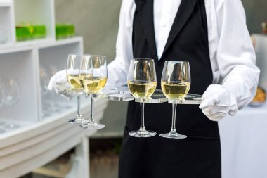 Açık büfe yemek partisinde şarap servisi yapan üniformalı profesyonel garsonun orta bölümü, şenlik ya da düğün. Tepside şampanya dolu bardaklar. Açık hava partisi yemek servisi, garsonluk.