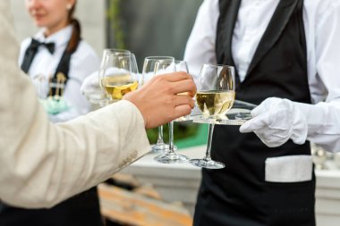 Açık büfe yemek partisinde şarap servisi yapan üniformalı profesyonel garsonun orta bölümü, şenlik ya da düğün. Tepside şampanya dolu bardaklar. Açık hava partisi yemek servisi, garsonluk.