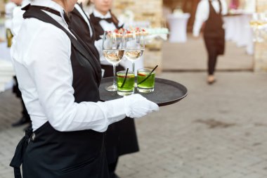 Açık büfe catering partisinde şarap, kokteyl ve abur cubur servisi yapan üniformalı profesyonel garsonların orta bölümü, şenlik ya da düğün. Tepside şarap dolu bardaklar. Açık hava parti yemek servisi.