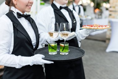 Açık büfe catering partisinde şarap, kokteyl ve abur cubur servisi yapan üniformalı profesyonel garsonların orta bölümü, şenlik ya da düğün. Tepside şarap dolu bardaklar. Açık hava parti yemek servisi.