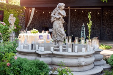 Heykeller ve mumlarla süslenmiş çeşme. Düğün töreni dekorasyonu detayları. Dışarıdaki restoranda heykelleri olan çeşme.