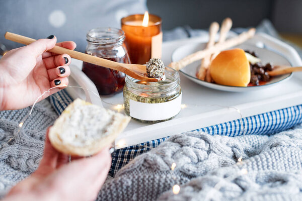Женские руки мажут сливочным сыром свежий хлеб. Завтрак в постель, поднос с сыром, гриссини, джем и ароматические свечи. Рождественское утро. Медовый месяц. Ранним утром в отеле