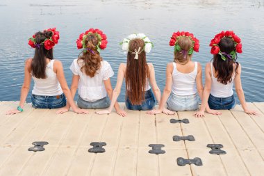 Çiçekli çelenkler, kot pantolonlar ve beyaz tişörtler giyen beş genç bayanın arkası. Bir grup arkadaş havuzun kenarında ya da iskelede oturuyorlar. Havuz partisi, yaz tatili. Web sitesi için pankart