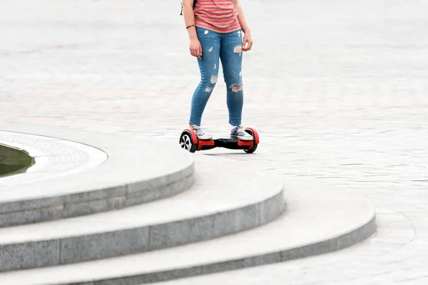 Young woman riding a hoverboard on the city square. New movement and transport technologies. Close up of dual wheel self balancing electric skateboard. People on electrical scooter outdoors