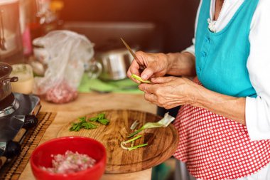 Kıdemli kadın mutfaktaki ahşap bir tahtanın üzerinde sebze doğrayan ellerini uzattı.