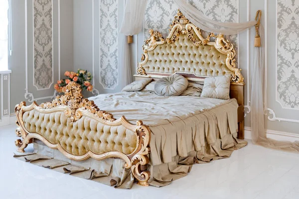 Luxury bedroom in light colors with golden furniture details. Big comfortable double royal bed in elegant classic interior.