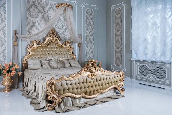 Luxury bedroom in light colors with golden furniture details. Big comfortable double royal bed in elegant classic interior.