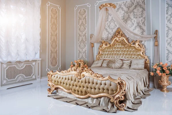 Luxury bedroom in light colors with golden furniture details. Big comfortable double royal bed in elegant classic interior.