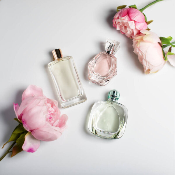 Perfume bottles with flowers on light background. Perfumery, cosmetics, fragrance collection. Flat lay.