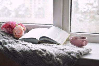 Samimi ev hayatı: bir fincan sıcak kahve, bahar çiçekleri ve pencere pervazında sıcak ekoseli bir kitap. İlkbahar konsepti, ücretsiz kopyalama alanı.