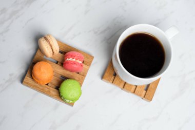 Küçük ahşap paletlerde servis edilen tatlı ve renkli badem kurabiyeleri ve mermer desenli arka planda bir fincan kahve. Geleneksel Fransız tatlısı.