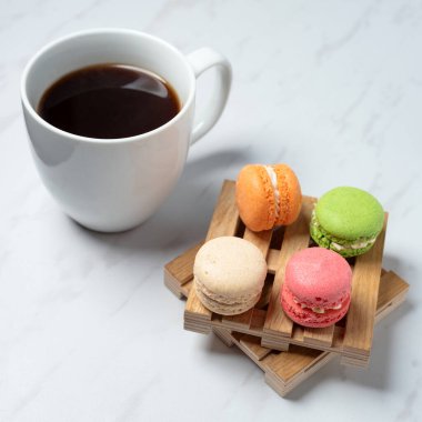 Küçük ahşap paletlerde servis edilen tatlı ve renkli badem kurabiyeleri ve mermer desenli arka planda bir fincan kahve. Geleneksel Fransız tatlısı.