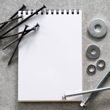 İnşaat aletleri. Vidalar, somunlar ve cıvatalar beton zemin üzerine yazılmış boş spiral ciltli kitap kağıtlarının etrafına dizilmiş. Tamir, ev geliştirme konsepti. Metin için boş alan, üst görünüm, düz uzanma