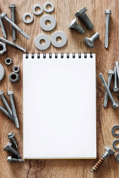 Construction tools. The screws, nuts and bolts arranged around blank spiral bound note book paper on wooden background. Repair, home improvement concept. Free space for text, top view, flat lay