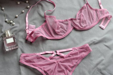 Gri çarşaflarda kadın aksesuarları olan göz kamaştırıcı seksi dantel iç çamaşırları. Tatil için yassı kadın esasları. İç çamaşırı, parfüm ve kolye. Alışveriş ve moda konsepti.