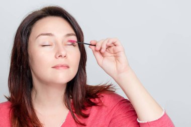 Makyaj yapan, kirpiklerini hazırlayan, kirpiklerini fırçalayan bir kadın. Tarama aşamasında kirpik bakımının kozmetik prosedürü. İnşa, boyama, kirpikleri kaplama.