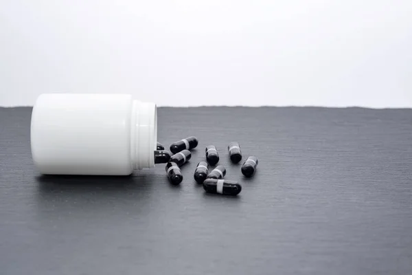 Black Supplement Capsules Poured White Bottle Slate Board Medicine Theme — Stock Photo, Image