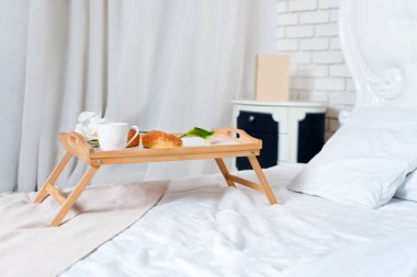 Yatakta kahvaltı, bir tepsi kahve, kruvasan ve çiçekler. Balayı. Çatı katında büyük boy bir yatak. Sabahın erken saatlerinde otelde.