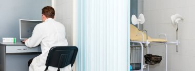 Ofiste bilgisayarını kullanan ve yazan bir doktor. Jinekoloji kürsüsü olan modern bir hastane. Jinekolog sıradaki hastayı bekliyor.