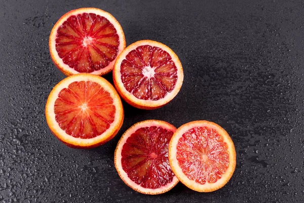 Blood oranges cut in half and sliced on black slate board with water drops. Red sicilian orange fruit. Top view, free space for text.