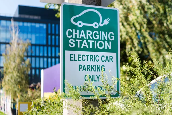 Electric car road sign charging station. Outdoor car parking and charging point for electric vehicle. Electric car charging station sign in front of public parking lot.