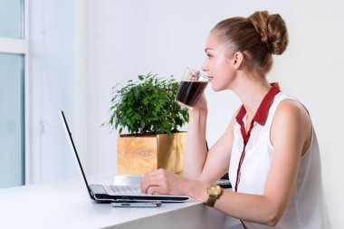 Young businesswoman in modern bright office with open notebook drinking hot morning coffee. Business concept