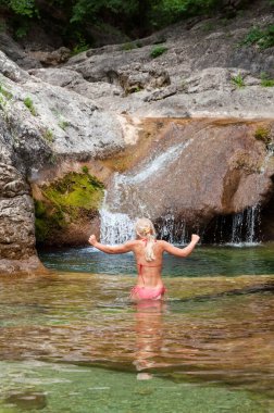 Güzel doğa, bikini mayo giyen kızın arkası güneşli yaz gününde gölde doğal şelalenin yanında mayo keyfi yapıyor..