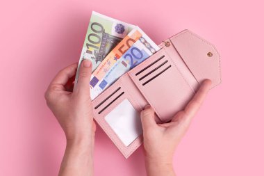 Cüzdanı tutan eller. Pembe deri cüzdan ve avroluk para kadınların elinde. Avrupa banknotlarını çantasından çıkaran ve devam eden bir kadının ellerine yakın çekim. Para kavramı, finans, alışveriş, nakit