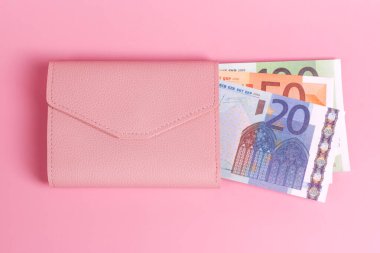 Pastel pembe arka planda, içinde avro banknotları olan pembe bir çanta. Modern deri cüzdan ve Avrupa banknotlarına yakın çekim. Finans, yatırım, tasarruf, nakit, zıplama ve ödeme konsepti. Üst görünüm.