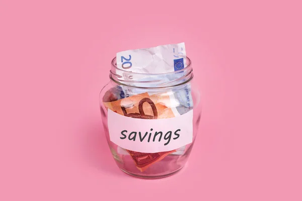 Euro banknotes in glass money jar with savings label, financial, saving. Money box with word SAVINGS on sticky note paper. Jar full of cash, save money concept, expense planning and control