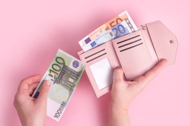 Cüzdanı tutan, parayı sayan ya da ödeyen eller. Pembe deri cüzdan ve avroluk para kadınların elinde. Kadının elleri Avrupa banknotlarını çantasından çıkarıyor. Para, finans, alışveriş. Boş kopyalama alanı