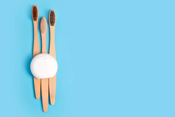 Dental floss containers and bamboo toothbrushes on blue background. Daily oral hygiene, teeth care and health. Cleaning products for mouth. Dental care concept. Empty place for text or logo.