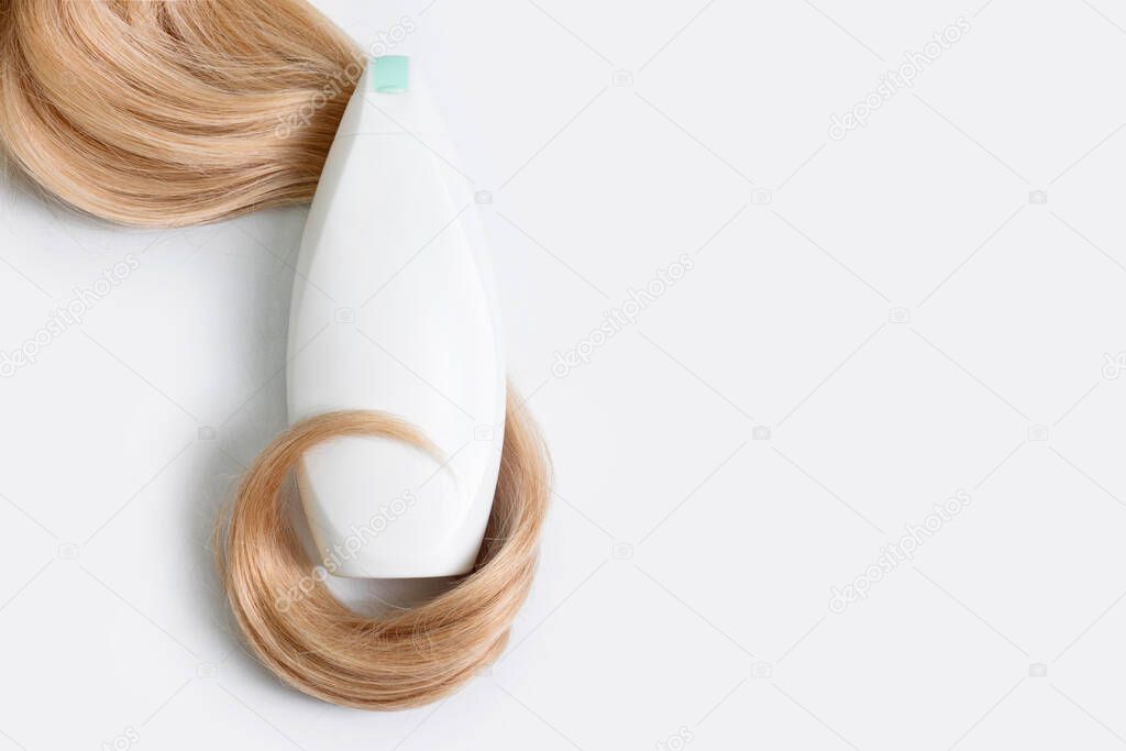 Shampoo or conditioner bottle wrapped in lock of curly blonde hair isolated on light background, top view. Flat lay, copy space for text. Hair care cosmetics, beauty haircare products, hair treatment