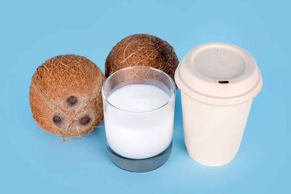 Noix de coco avec un verre de lait de coco et une tasse de café en papier sur fond bleu. Aliments végétaliens sains, régime sans lactose, alternative au lait, café à emporter, latte végétalien ou cappuccino à la noix de coco. — Photo