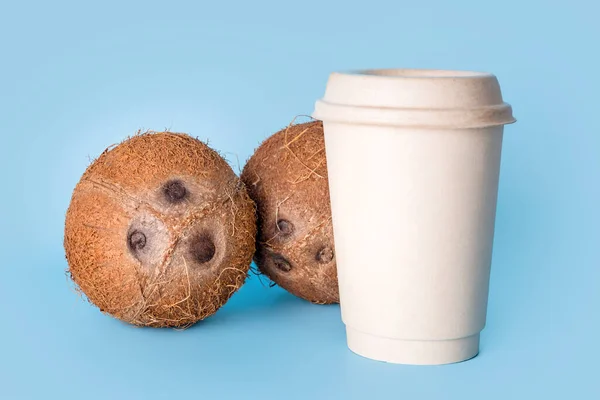 青い背景に紙コーヒーカップとココナッツ 健康的なビーガンフード 乳糖フリーダイエット ミルク代替 移動するコーヒー ビーガンラテやココナッツカプチーノ — ストック写真