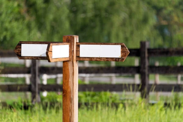 Empty wooden sign with arrows on the ranch. Simple wooden triple direction arrow roadsign in the gargen with wooden fence