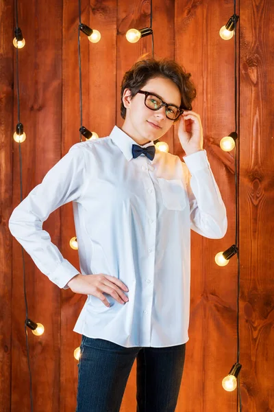 Adolescente inteligente usando óculos posando no apartamento loft. Menina adolescente em camisa branca no fundo lâmpadas — Fotografia de Stock