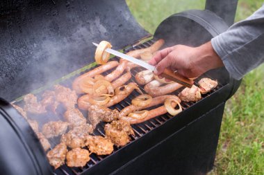 Yeşil çimlerin üzerinde et ve sosisler ızgarada. Adam yemek yapıyor..