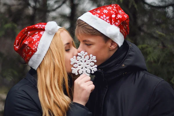 Mutlu genç çift öpüşme ve büyük bir kar tanesi tutan Santa şapka giymiş aşık. Erkek ve kadın Noel ve yeni yıl kutlama