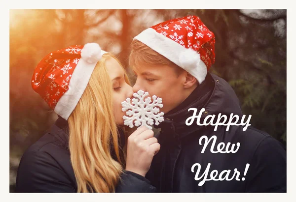 Happy young couple in love wearing Santa hats kissing and holding a big snowflake. Man and woman celebrating Christmas and New Year. Retro vintage instagram filter — Stock Photo, Image