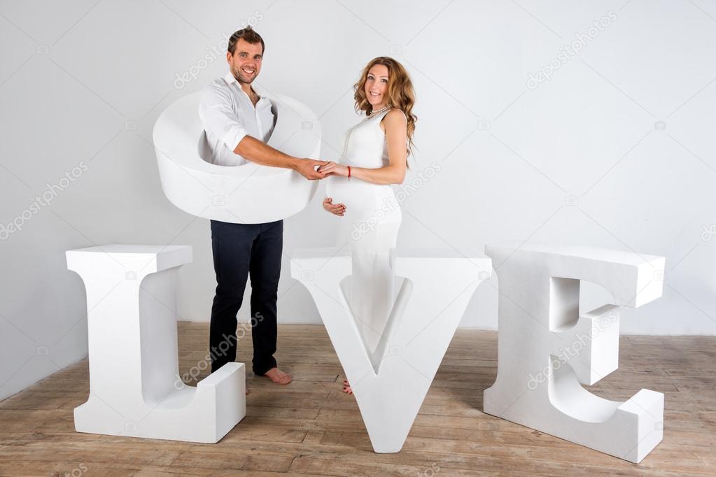Happy Pregnant Couple dressed in white on white background with giant handmade letters of the word love