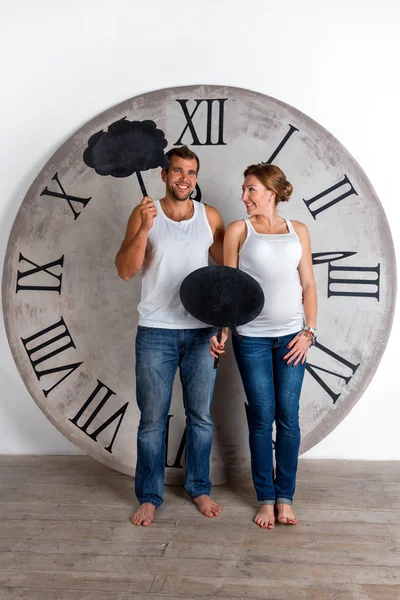 Happy Pregnant Couple dressed in white showing sign speech bubble banners looking happy excited and having idea on white background with giant clock. — Stock Photo, Image
