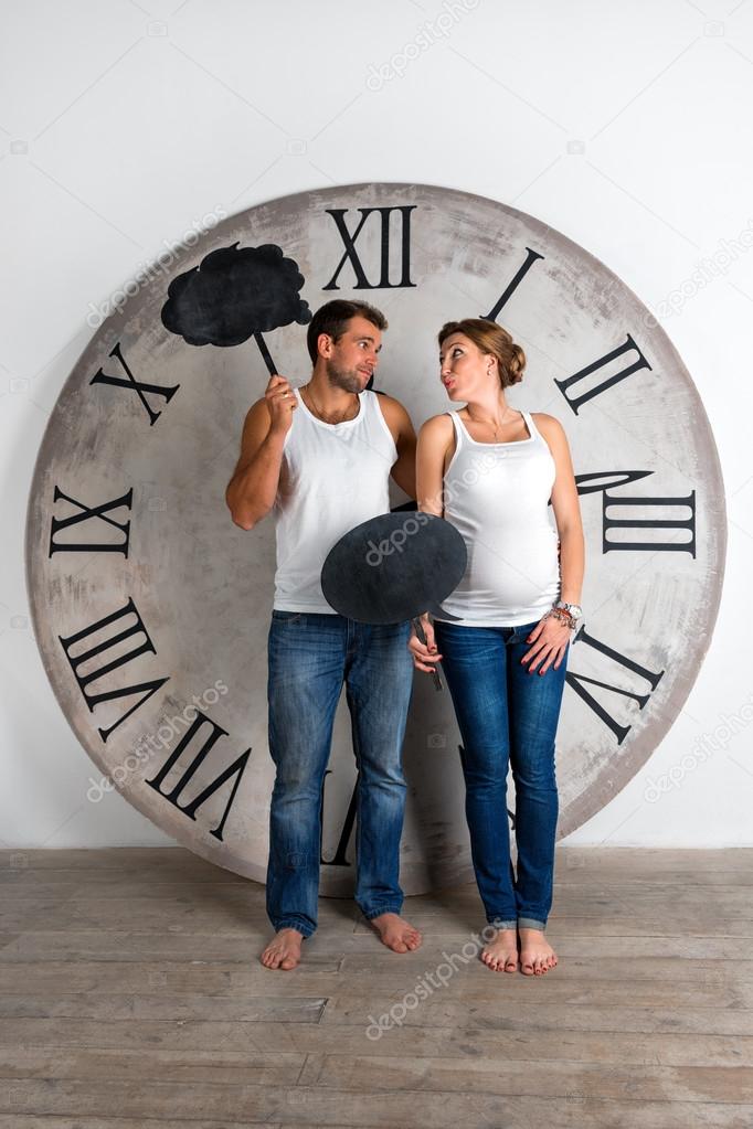 Happy Pregnant Couple dressed in white showing sign speech bubble banners looking happy excited and having idea on white background with giant clock.