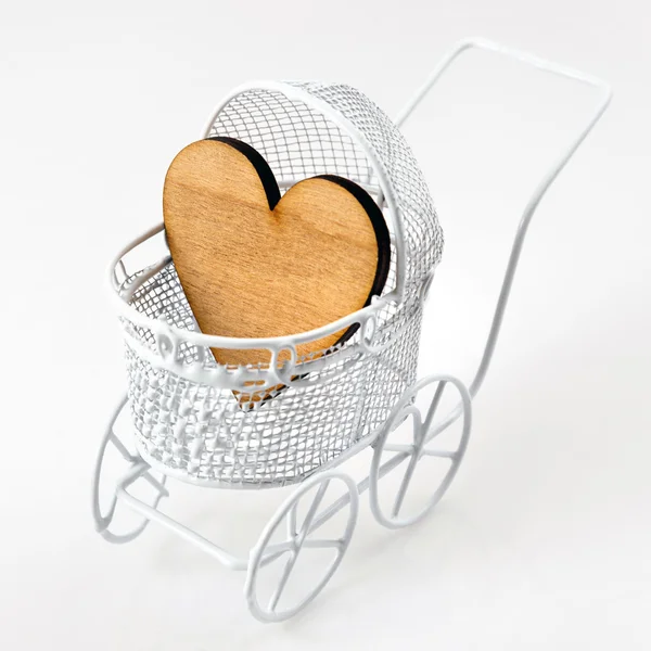 Wózek z drewnianym sercem na białym tle. Noworodka kartkę z życzeniami. — Zdjęcie stockowe